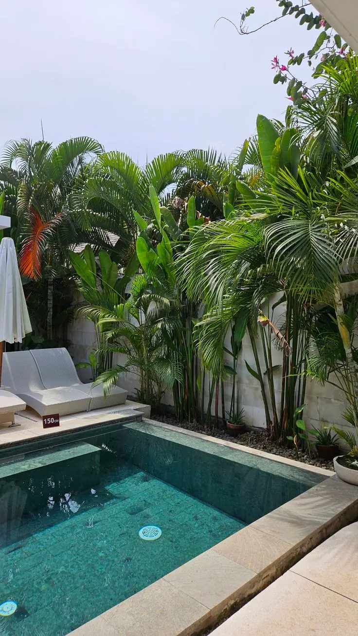 Piscina revestida de piedra verde junto a un jardín tropical con tumbona blanca